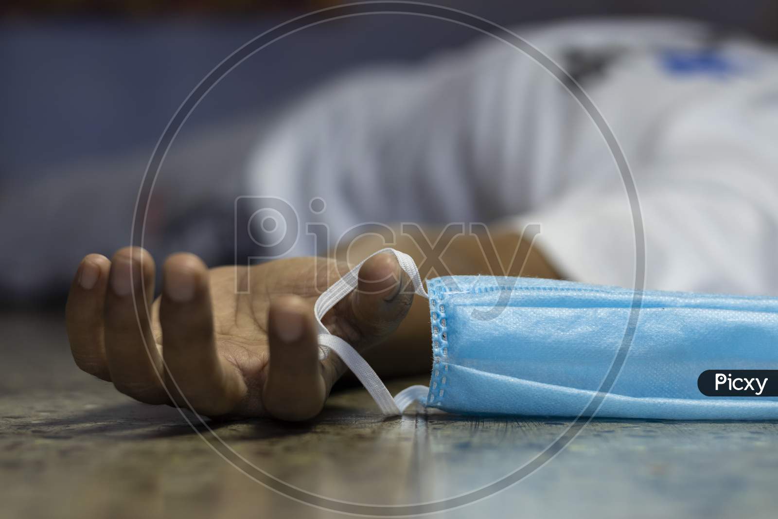 An Indian Or Asian Person Laying On Floor Dead Holding A Nose Mask During Covid-19 Or Corona Virus Outbreak With Selective Focus Or Shallow Depth Of Field