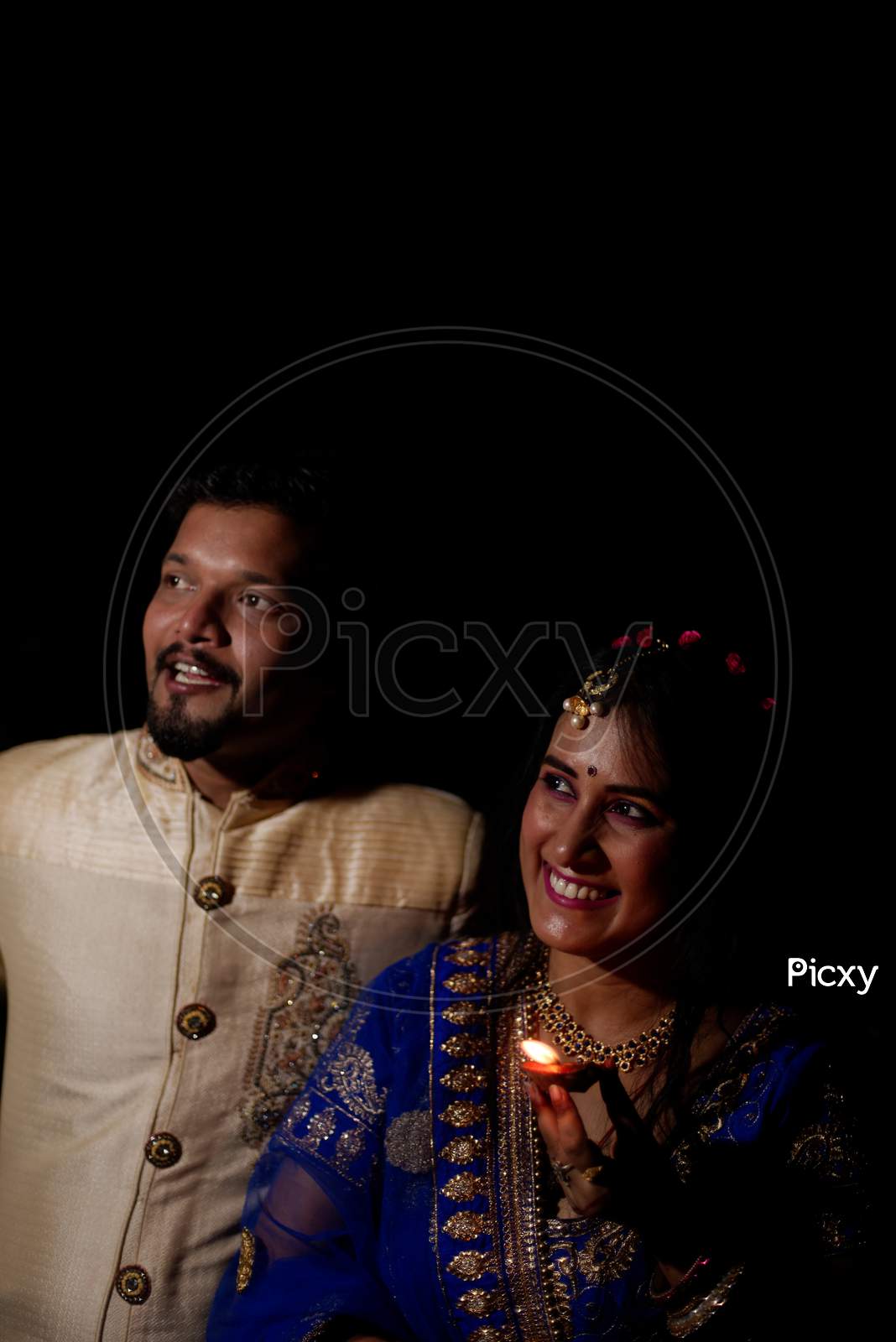 Young and beautiful Indian Gujarati couple in Indian traditional dress celebrating Diwali with diyas/lamps on the terrace in darkness on Diwali evening. Indian lifestyle and Diwali celebration