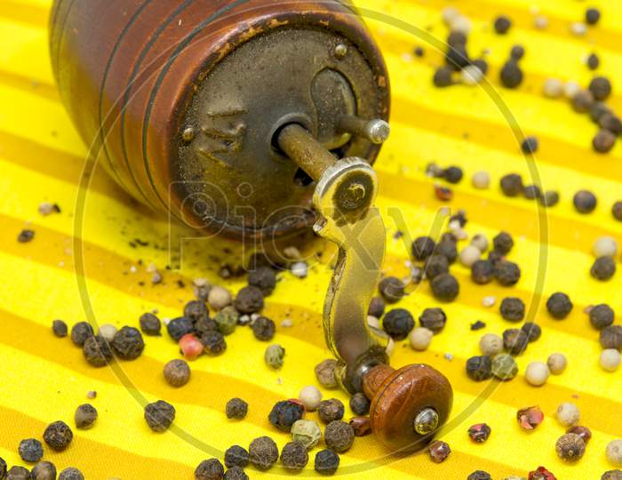old pepper grinder and assorted pepper whole grains and ground pepper on yellow cloth