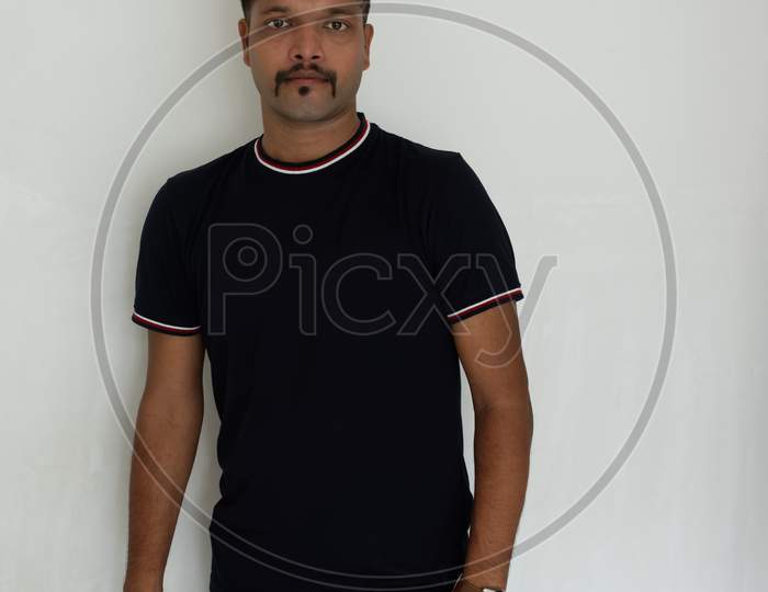 Close up portrait of a handsome and intelligent Indian brunette man wearing a solid black t shirt standing before a copy space white background. Indian lifestyle and fashion portrait