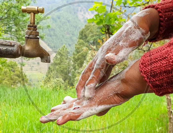 capture of a woman rubbing hands with soap in outdoor with greenery in background in hilly area of Himachal Pradesh, India