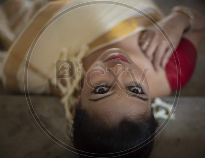 An young and attractive Indian woman in white traditional sari and red blouse and flowers is smiling while Lying On Steps  for the celebration of Onam/Pongal. Indian lifestyle.