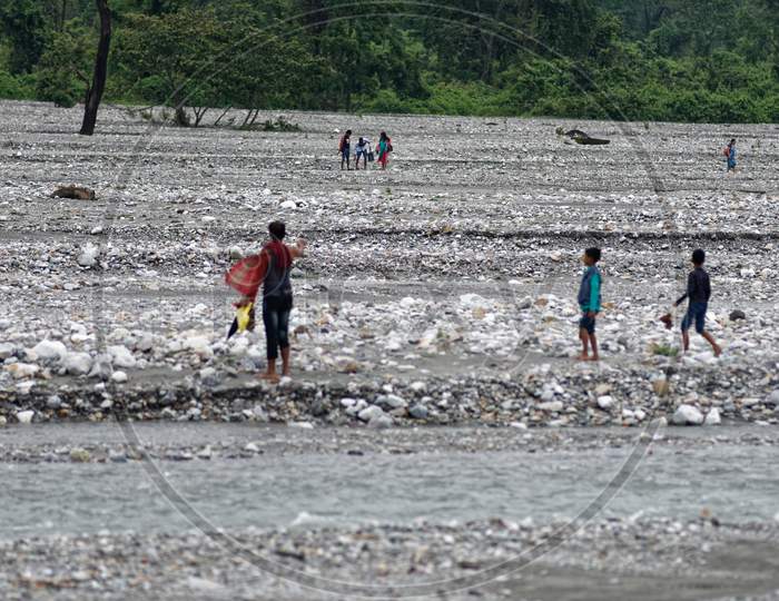 Indian people are walking by the pebbles beside the river bank of a dried river bed. Indian lifestyle