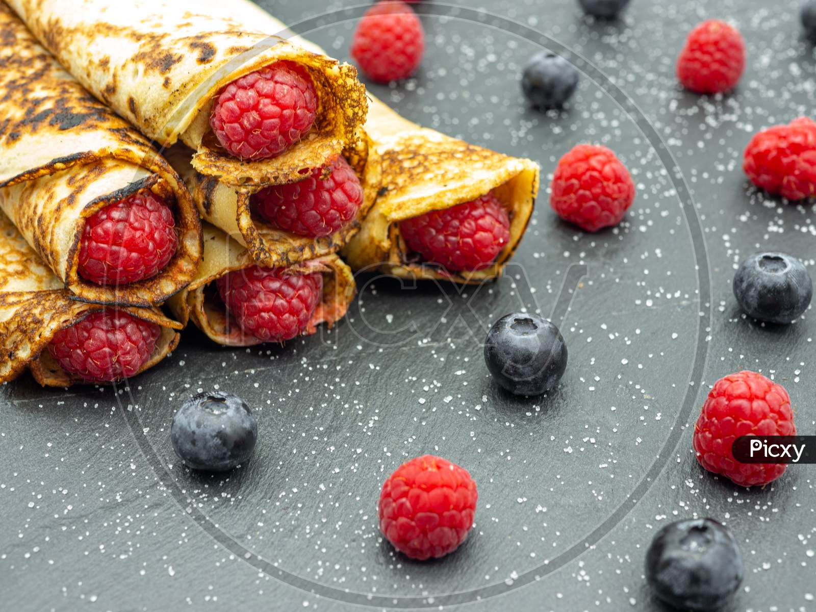 Crepes filled with jam and fresh raspberry and blueberries on black slate