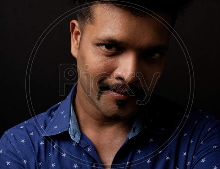 Close up portrait of a handsome and intelligent Indian brunette man in his specs wearing blue shirt with white stars. Indian lifestyle and fashion portrait
