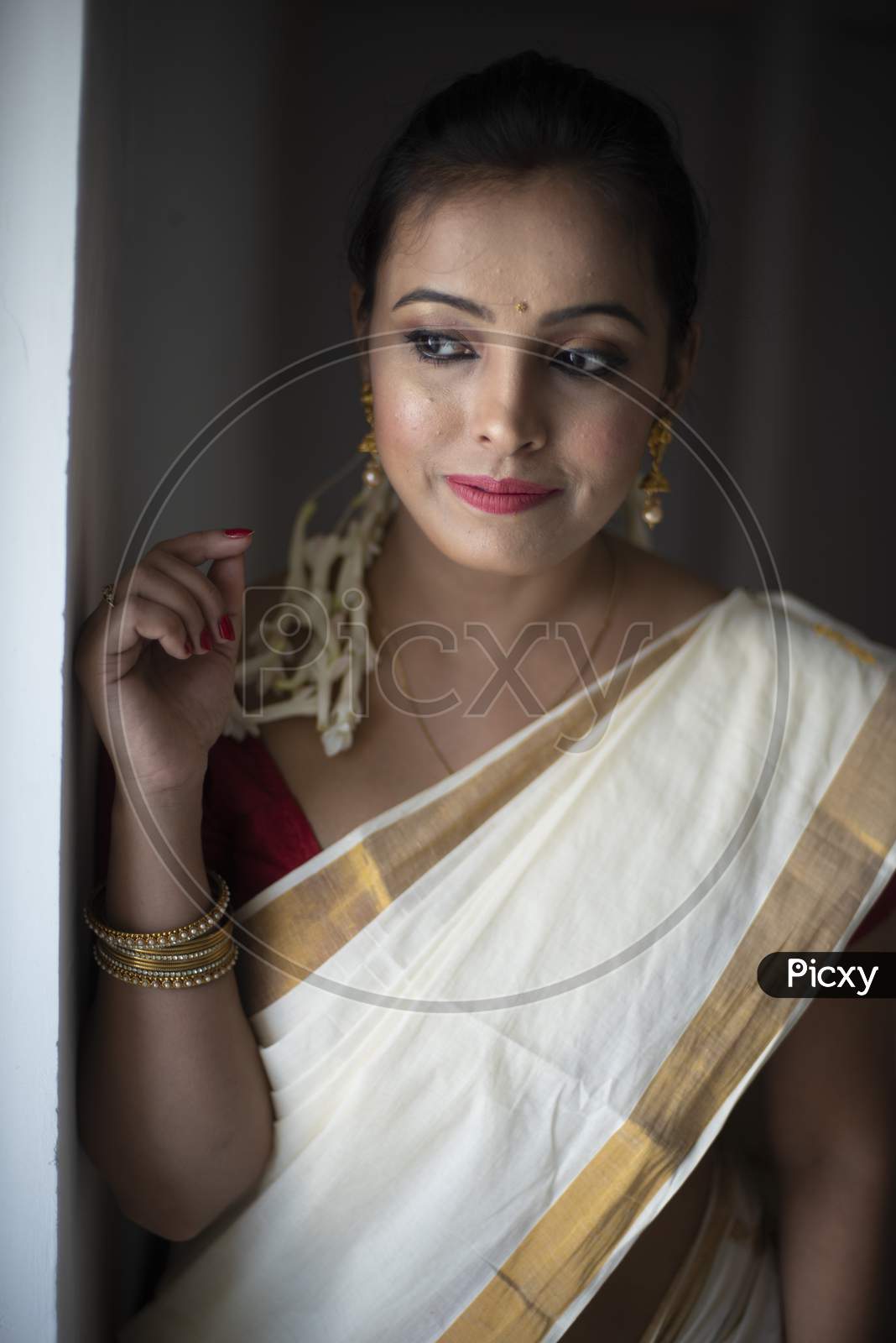 An young and attractive Indian woman in white traditional sari and red blouse and flowers is smiling while Standing at a Balcony and Posing   for the celebration of Onam/Pongal. Indian lifestyle.