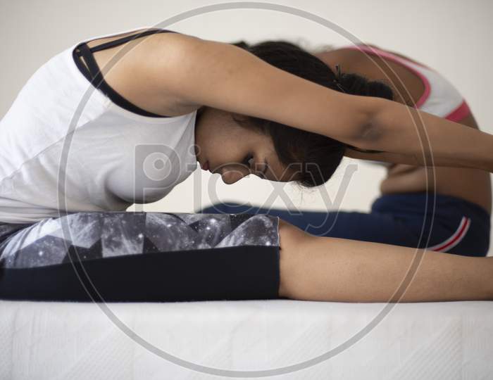 Indian black and white brunette girls are performing yoga/sports /exercise in sportswear in front of a white background. Indian lifestyle