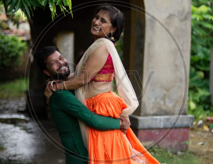 Young and attractive Indian Bengali brunette couple standing in front of a vintage house hugging each other  romantically wearing Indian traditional ethnic cloths. Indian lifestyle and fashion