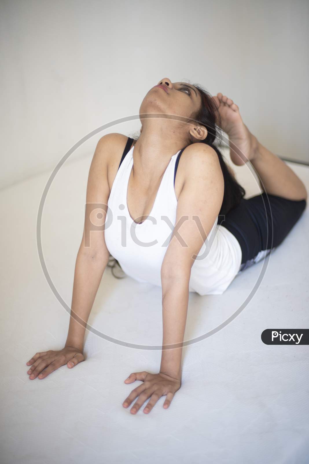 Indian brunette girl performing yoga/sports /exercise in sportswear in front of a white background. Indian lifestyle