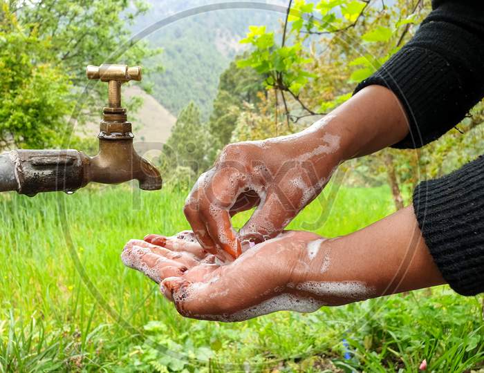 capture of a woman rubbing hands with soap in outdoor with greenery in background in hilly area