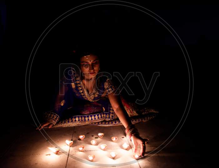 Young and beautiful Indian Gujarati woman in Indian traditional dress celebrating Diwali with illuminated diya/lamps on rooftop on Diwali evening. Indian lifestyle and Diwali celebration