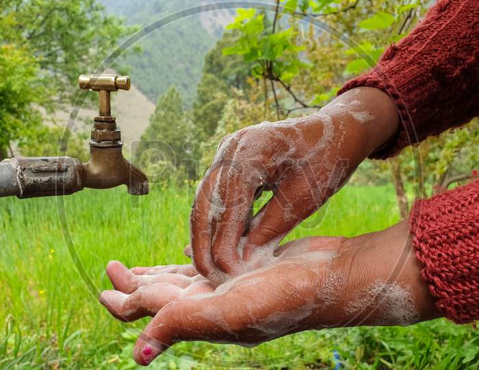 capture of a woman rubbing hands with soap in outdoor with greenery in background in hilly area of Himachal Pradesh, India