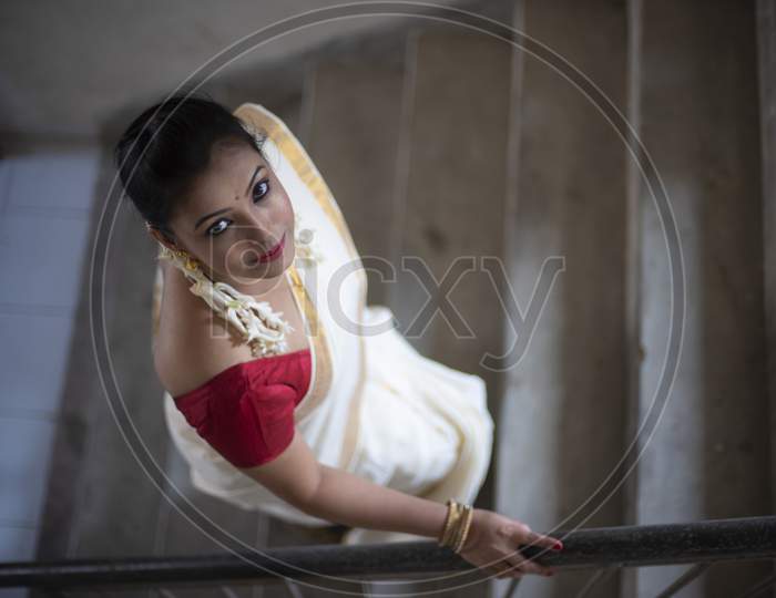 An young and attractive Indian woman in white traditional sari and red blouse and flowers is Walking on Steps or Stairs for the celebration of Onam/Pongal. Indian lifestyle.