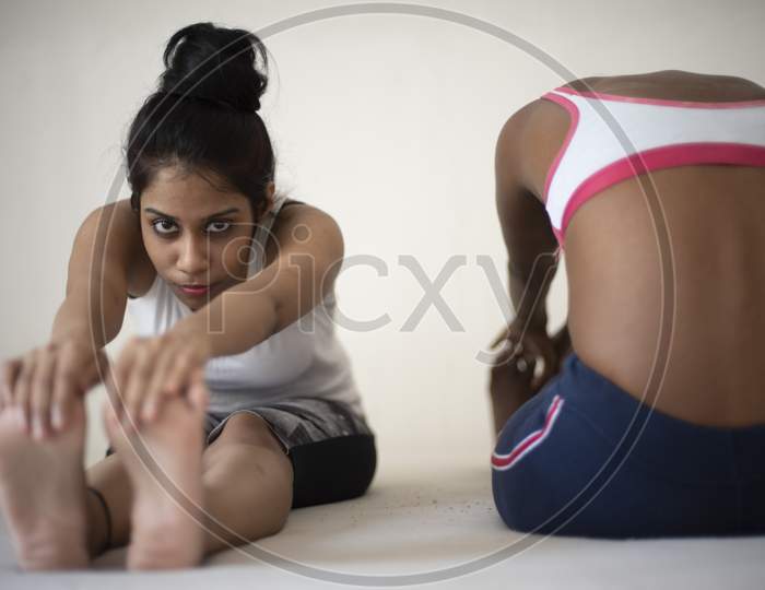 Indian black and white brunette girls are performing yoga/sports /exercise in sportswear in front of a white background. Indian lifestyle