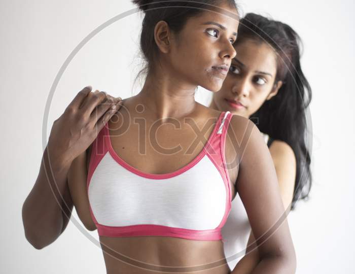 A beautiful and young Indian Bengali lesbian couple in sports inner/underwear are interacting in a intimate way in front of a white background. Dark and fare model, Indian lifestyle