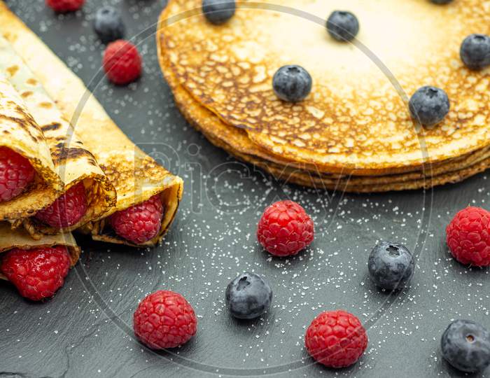 Crepes filled with jam and fresh raspberry and blueberries on black slate