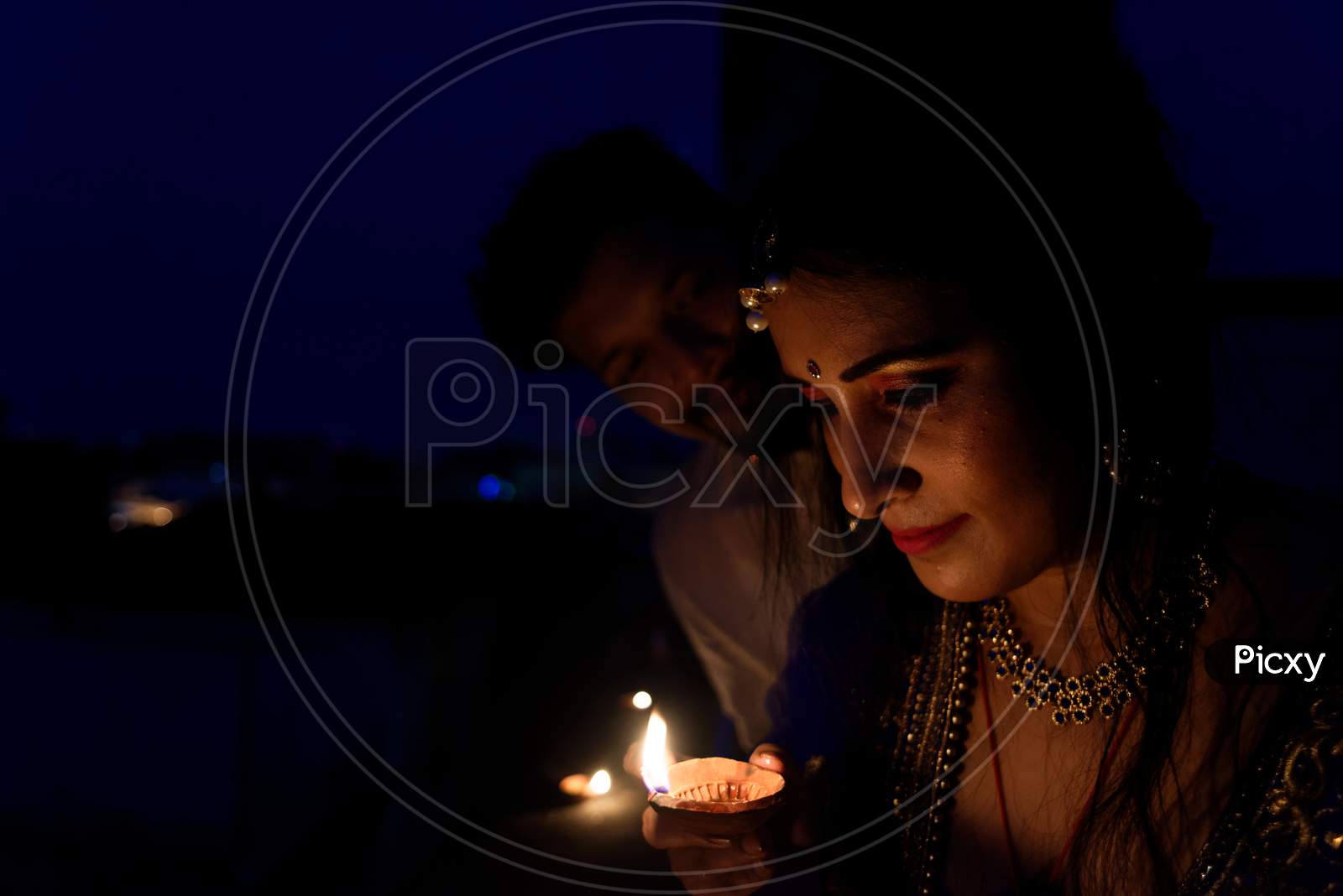 Young and beautiful Indian Gujarati couple in Indian traditional dress lightening Diwali diya/lamps on the terrace in darkness on Diwali evening. Indian lifestyle and Diwali celebration
