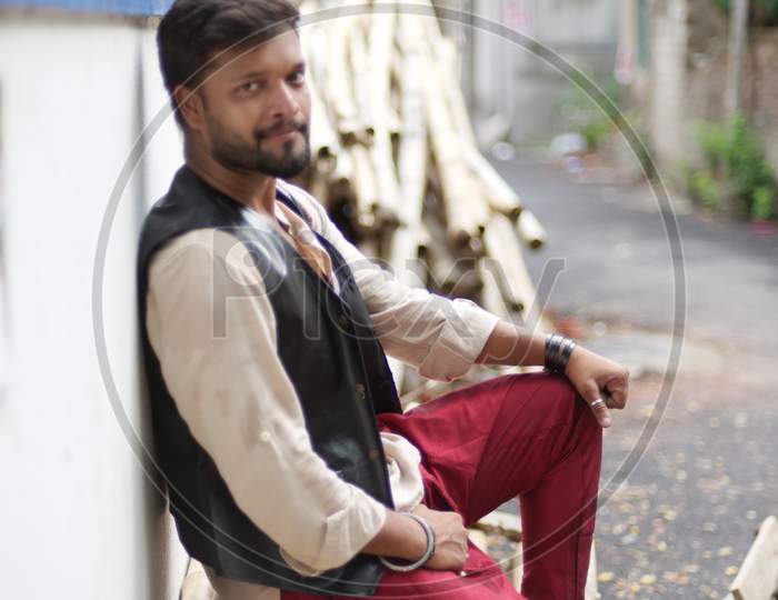 portrait of young and handsome Indian Bengali brunette beard man posing on street leaning on a wall wearing Indian ethnic vibrant jacket, shirt and red pant. Indian lifestyle and fashion
