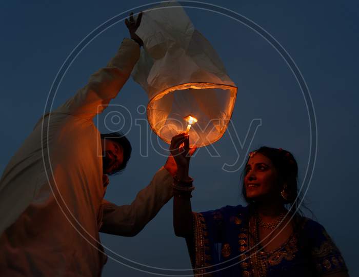 An Indian Bengali couple is celebrating Diwali by lighting flying lanterns in the sky in blue hour. Indian lifestyle and Diwali celebration