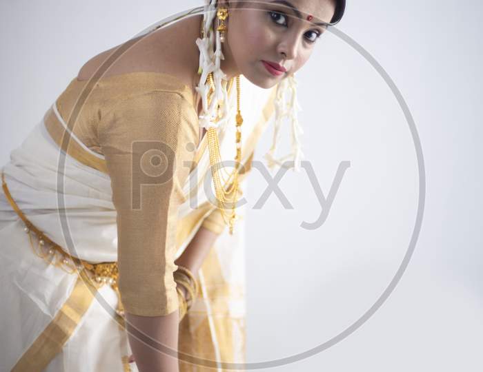 Portrait of an young and attractive Indian woman in white traditional wear with colorful flowers in hands for the celebration of Onam/Pongal in white background. Indian lifestyle
