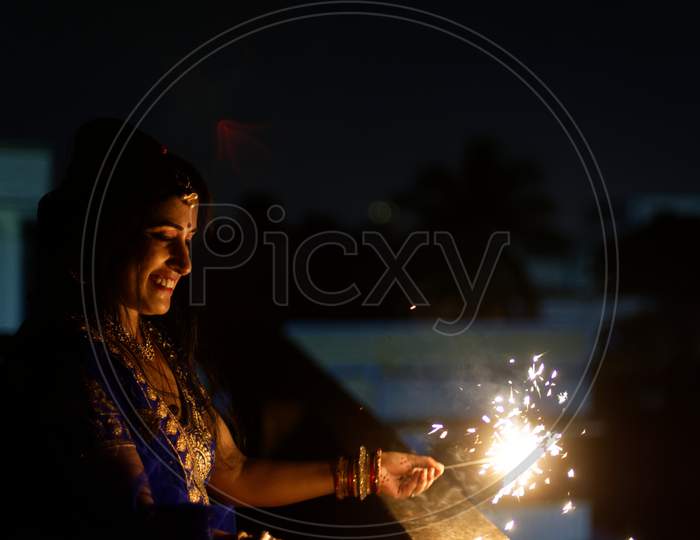 Young and beautiful Indian Bengali/gujarati/rajasthani woman in Indian traditional dress is celebrating Diwali with fire crackers on rooftop in darkness. Indian lifestyle and Diwali celebration