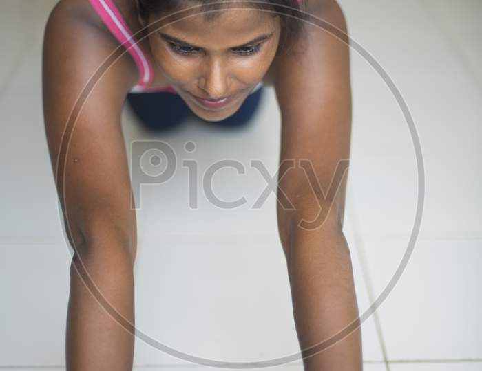 Side posture of an Indian dark skinned brunette girl in sportswear performing exercise with ab roller in front of glass window in a white background. Indian lifestyle
