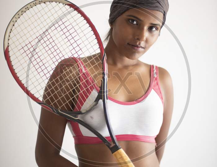 Portrait of an attractive young brunette dark skinned Indian Bengali girl in western sportswear and a tennis bat in a balcony in white background. Indian lifestyle
