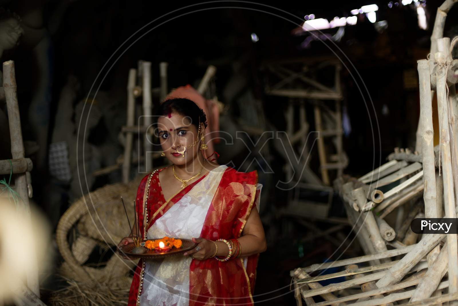 An young and beautiful Indian Bengali brunette woman in red white traditional ethnic sari holding a puja thali for worshiping goddess Durga clay idol . Indian culture, religion and fashion