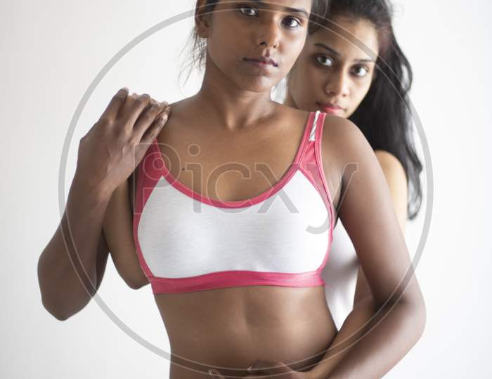 A beautiful and young Indian Bengali lesbian couple in sports inner/underwear are interacting in a intimate way in front of a white background. Dark and fare model, Indian lifestyle