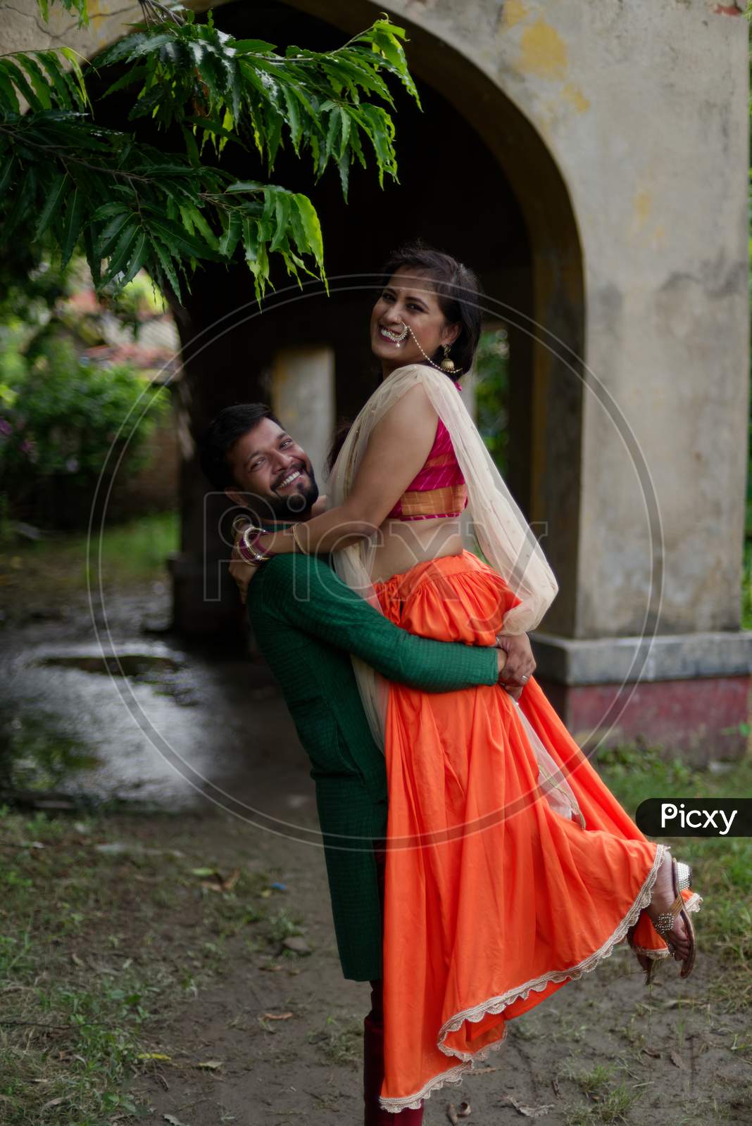 Young and attractive Indian Bengali brunette couple standing in front of a vintage house hugging each other  romantically wearing Indian traditional ethnic cloths. Indian lifestyle and fashion