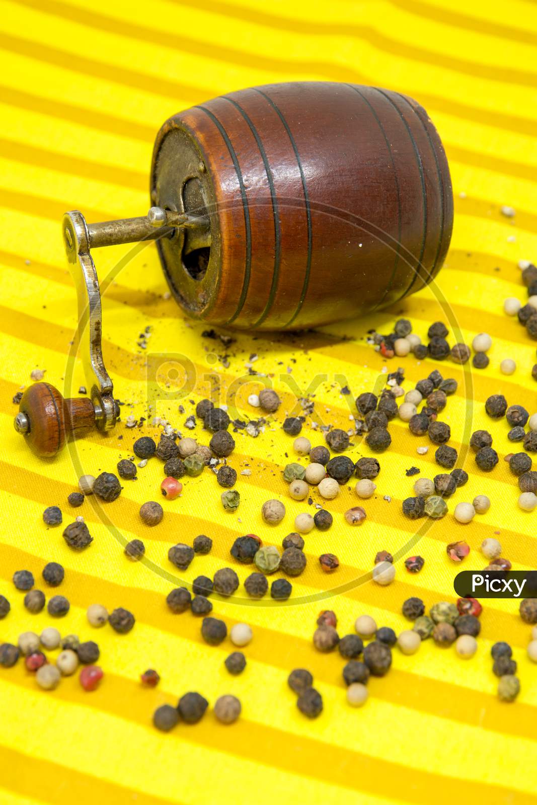 old pepper grinder and assorted pepper whole grains and ground pepper on yellow cloth