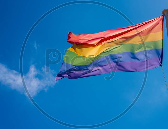 LGBT pride flag hung on a mast and waving in the blue sky