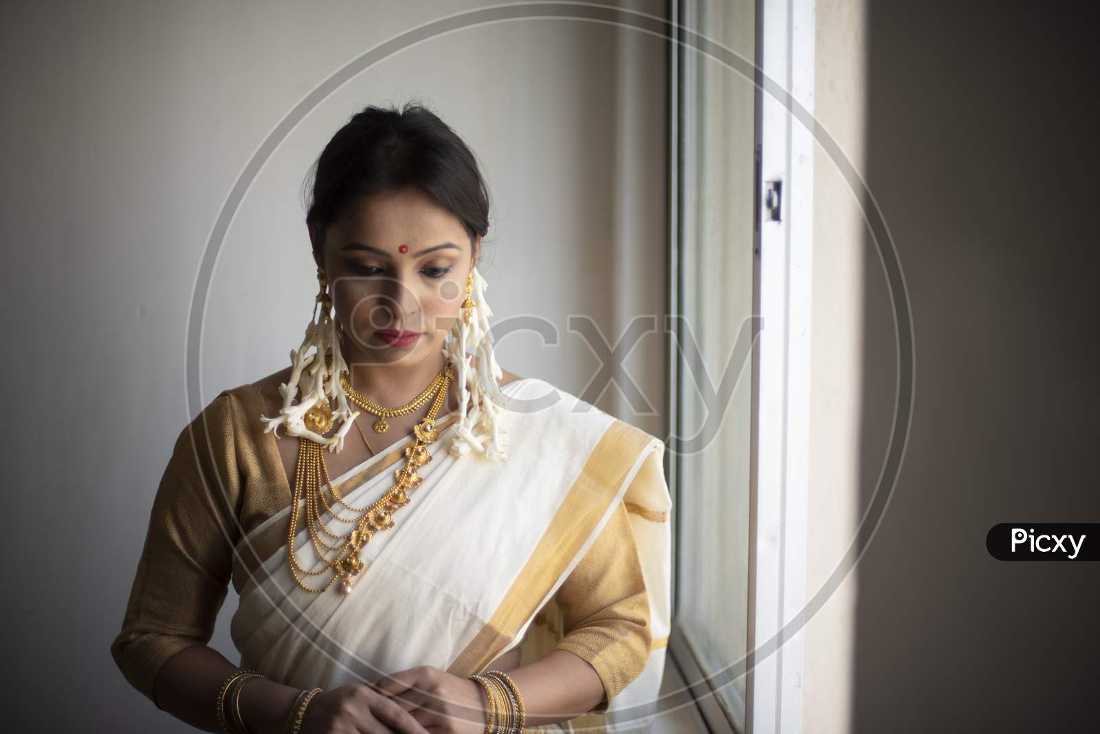 An young and attractive Indian woman in white traditional sari and red blouse and flowers is standing in a balcony for the celebration of Onam/Pongal. Indian lifestyle.