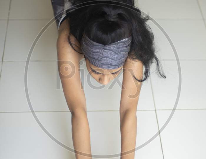 posture of an Indian brunette girl in sportswear performing exercise with ab roller in front of glass window in a white background. Indian lifestyle