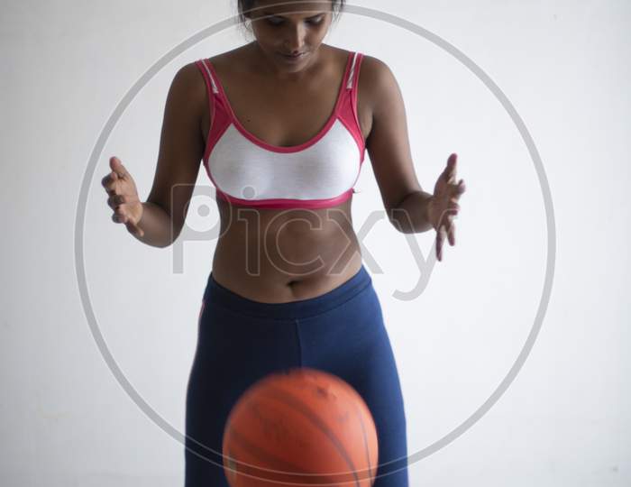 Portrait of an attractive young brunette dark skinned Indian Bengali girl in western sportswear and an orange basketball in front of white studio background. Indian lifestyle