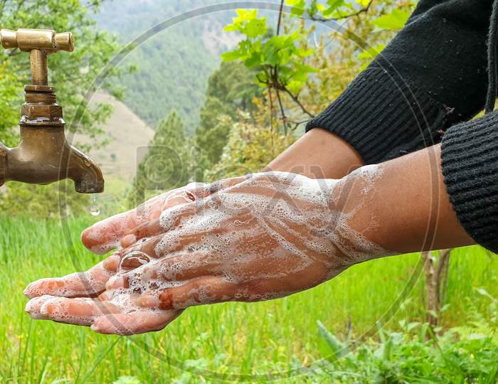 capture of a woman rubbing hands with soap in outdoor with greenery in background in hilly area