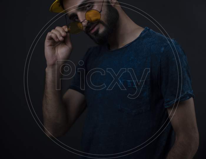 Portrait of young brunette Indian/European/Arabian/Kashmiri man in casual tee shirt with sunglasses and yellow hat in black copy space studio background. lifestyle and fashion.