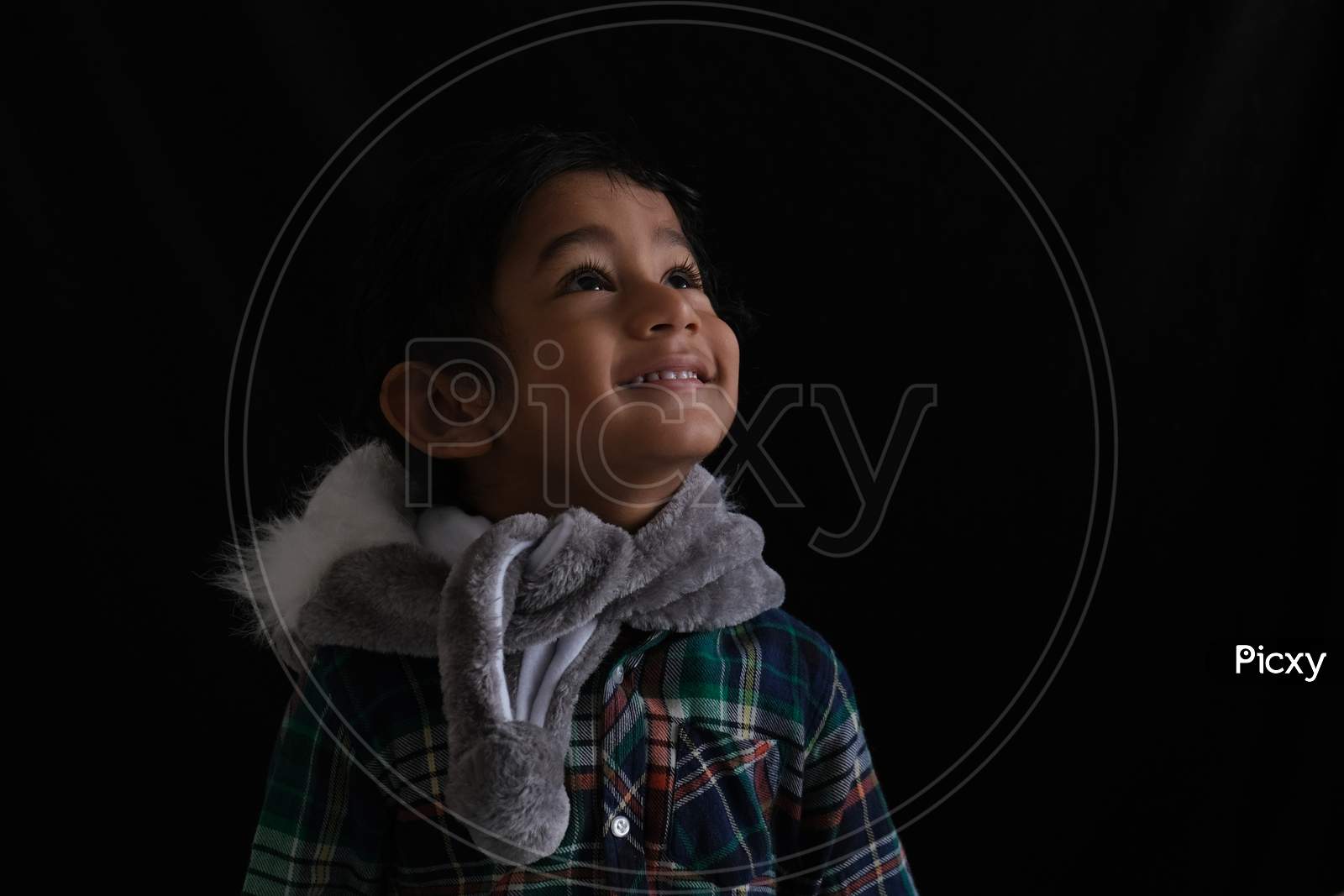 Portrait of Indian cute little cheerful brunette Tamil baby boy wearing casual dress with a furry toy in a black background. Indian lifestyle.