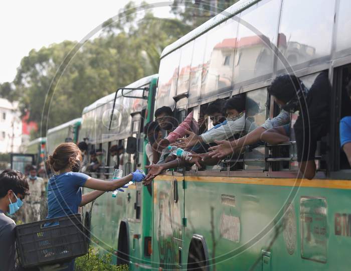 A woman provides bottles of drinking water to men inside a bus as they wait to alight to board a special train arranged by the government to repatriate migrant workers from the Chikkabanavara Junction Railway Station on the outskirts of Bangalore, India.