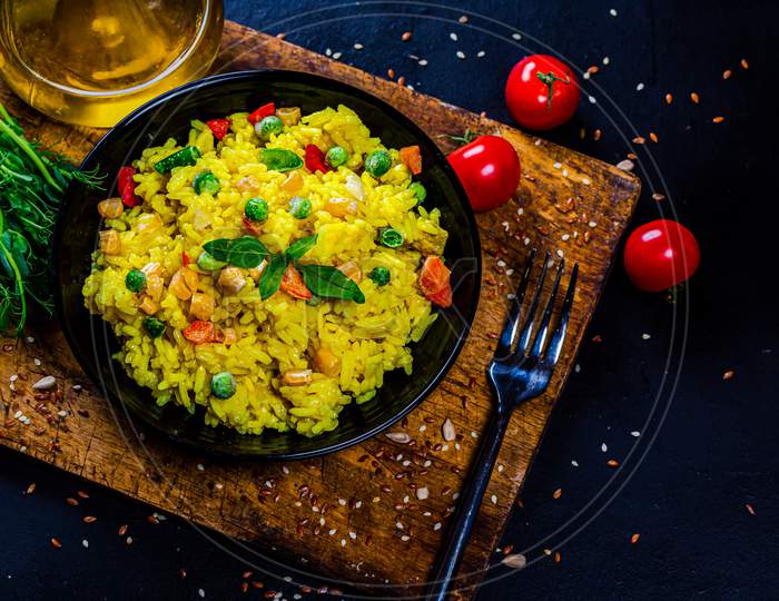yellow rice with vegetables and greens in a black bowl with wooden background