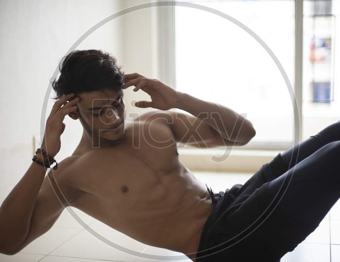 An young and handsome Indian Bengali brunette man with muscular body doing exercise in a room in white background. Fitness and Indian lifestyle.