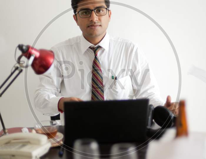 Indian Bengali tall, dark, handsome brunette young man in office wear enjoying success while sitting on an office table  in a corporate office/bpo/call center. Indian corporate lifestyle.