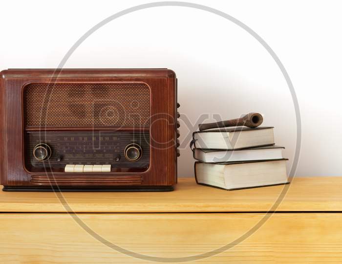 Vintage radio made of wood, old books and a pipe on a table