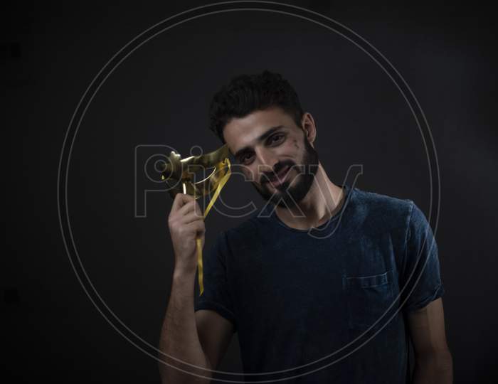 Portrait of young brunette Indian/European/Arabian/Kashmiri man in casual tee shirt holding a golden mask in black copy space studio background. lifestyle and fashion.