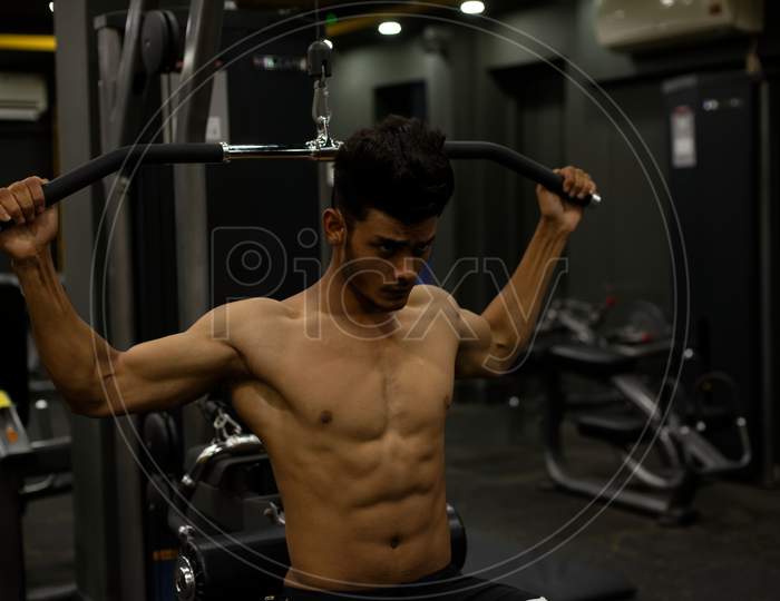 Portrait of an young and handsome Indian Bengali brunette man with muscular body doing exercise in a multi gym. Indian lifestyle