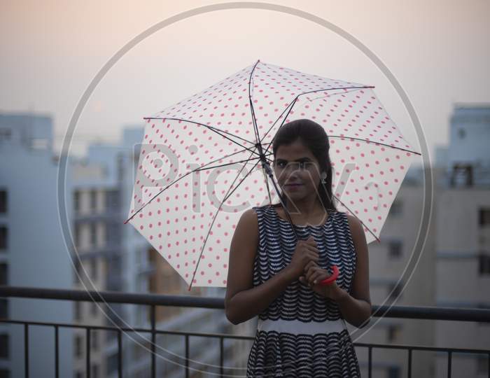 Portrait of a young dark skinned Indian/African girl in western dress standing with umbrella on a rooftop in the afternoon in urban background. Indian lifestyle.