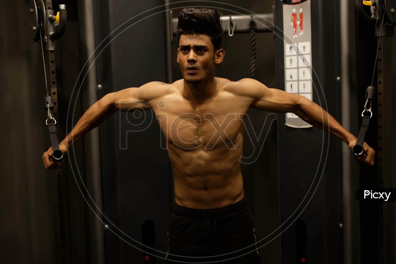 An young and handsome Indian Bengali brunette man with muscular body doing exercise in a multi gym. Fitness and Indian lifestyle.