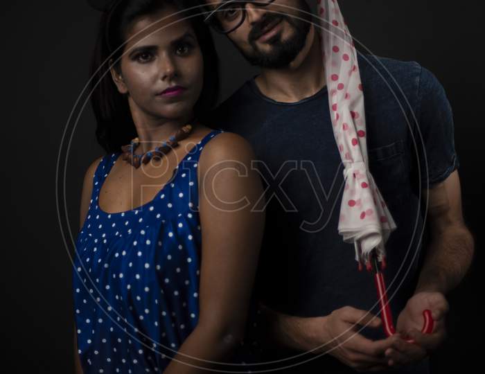 A dark skinned Indian/African girl floral western dress and a Kashmiri/European/Arabian man in casual wear with an umbrella in front of black copy space studio background. Indian lifestyle.