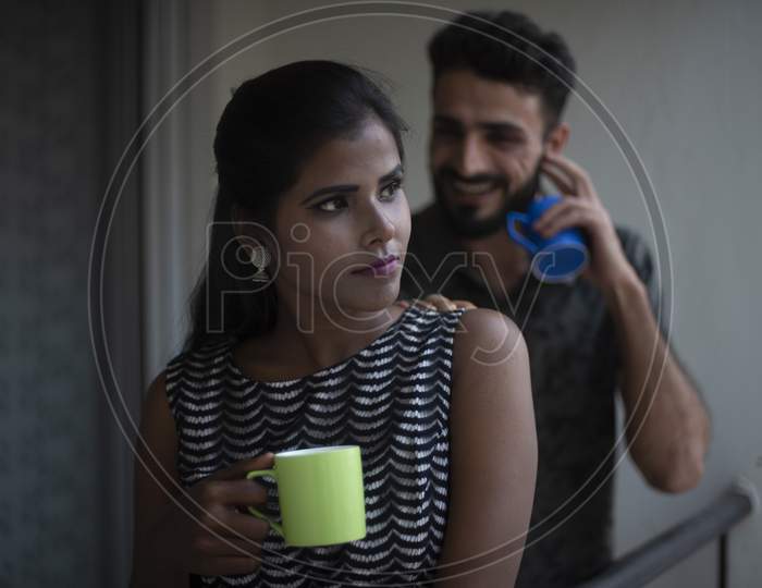A dark skinned Indian/African girl in  western dress and a Kashmiri/European/Arabian man in casual wear spending time with coffee/tea on a balcony in white background. Indian lifestyle.
