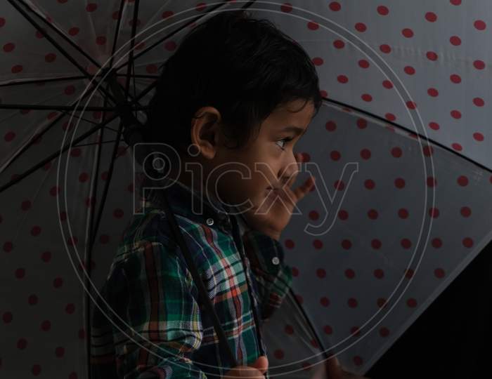 Portrait of Indian cute little cheerful brunette Tamil baby boy wearing casual dress with an umbrella in a black background. Indian lifestyle.